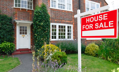 A brick house with a well-maintained garden and a "House For Sale" sign in the front yard.